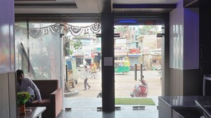 A lobby with a reception desk, a sofa, and a view of the street outside. - TRPOTEL SUBMANGAL (Gwalior)