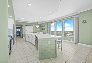 A spacious kitchen with a large island, a dining area with chairs, and a view through large windows. - Unit 1601: 16th Floor (Panama City Beach)