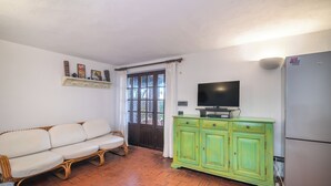 Ein Wohnzimmer mit einer Couch, einem Fernseher auf einem Schrank, einem grünen Schrank und einem Kühlschrank.