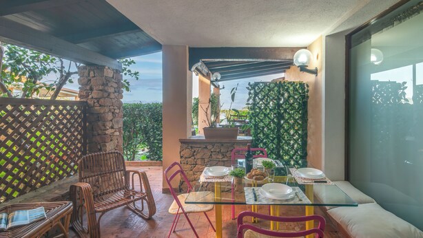 Ein Patio mit einem Glastisch, Korbstühlen und einer Stein Säule.