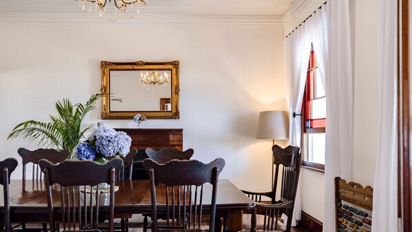 A dining room with a wooden table, six chairs, a chandelier, a mirror, and a window with curtains.