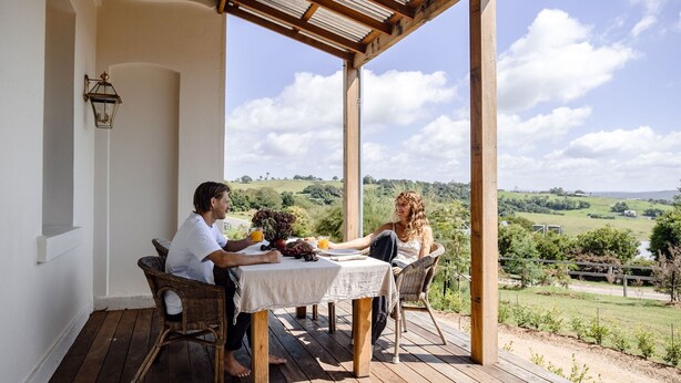 A covered outdoor dining area with a table set for two, overlooking a rural landscape.