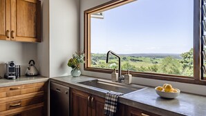 A kitchen with wooden cabinets, a stainless steel sink, a kettle, a vase with flowers, and a bowl of lemons.