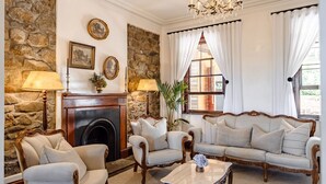 A room with a stone wall, a fireplace, a sofa, two armchairs, a coffee table, and a chandelier.