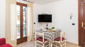 Un comedor con una mesa preparada para dos personas, un televisor montado en la pared y una puerta a la derecha.