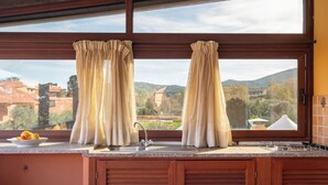 A kitchen with a large window, wooden cabinets, a sink, and a bowl of lemons on the counter. - Trilocale H Ginepro Sgombro (Olbia)