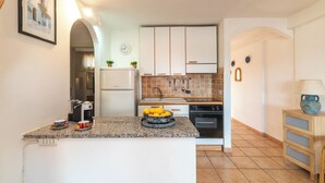 A kitchen with white cabinets, a granite countertop, and a sink. There are two potted plants on the wall above the sink. - Trilocale H Ginepro Sgombro (Olbia)