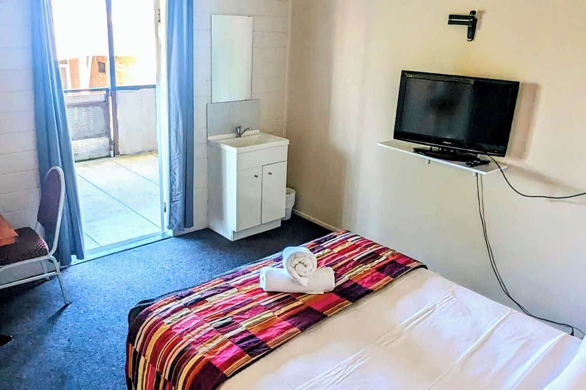 A hotel room with a bed, a TV mounted on the wall, a small white cabinet, and a window with curtains.
