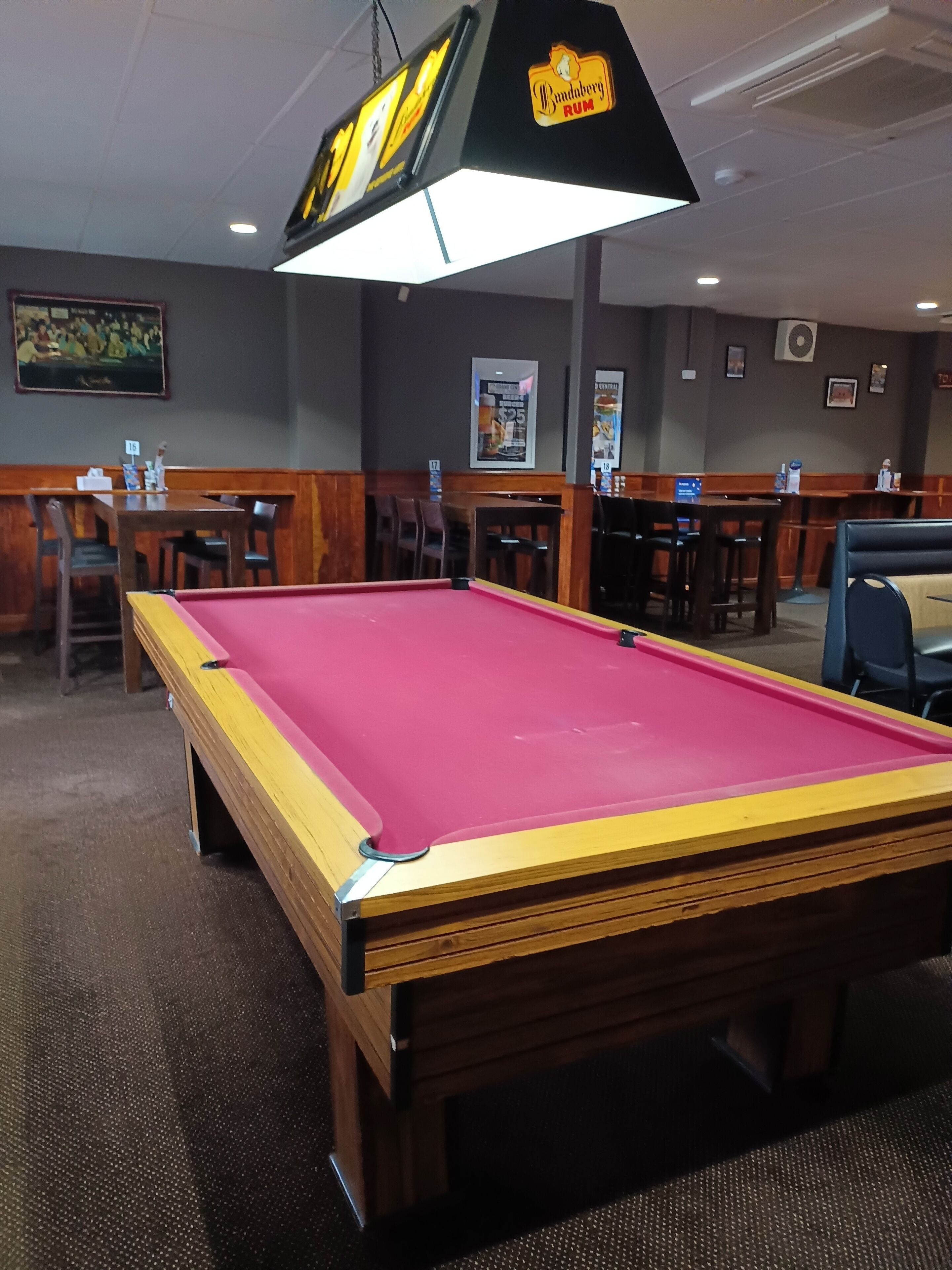 A pool table in a room with wooden furniture, a sign for Bambuerg Rum, and a framed picture on the wall.