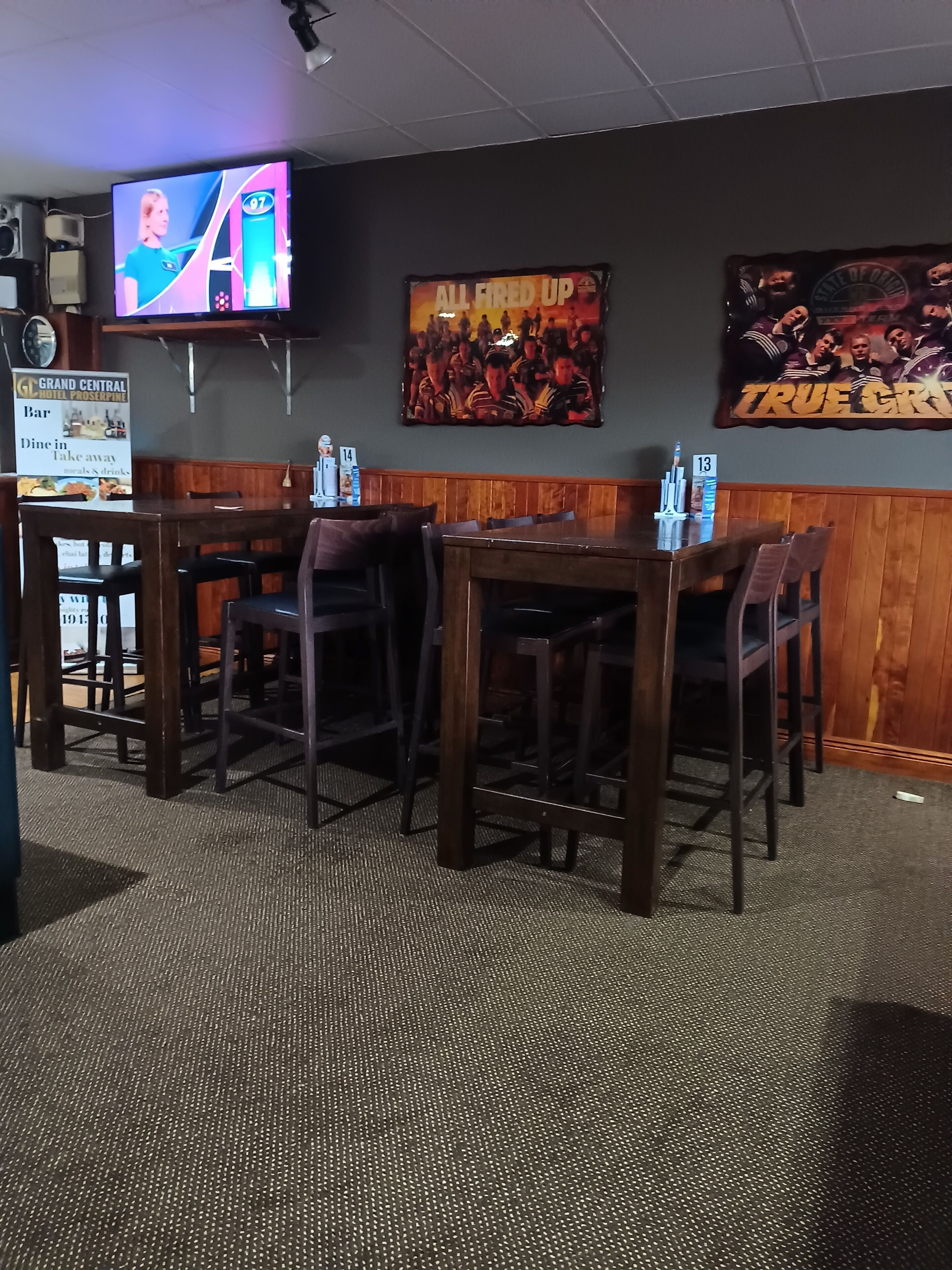 A restaurant with wooden booths and tables, a TV screen displaying a sports event, and posters on the wall.