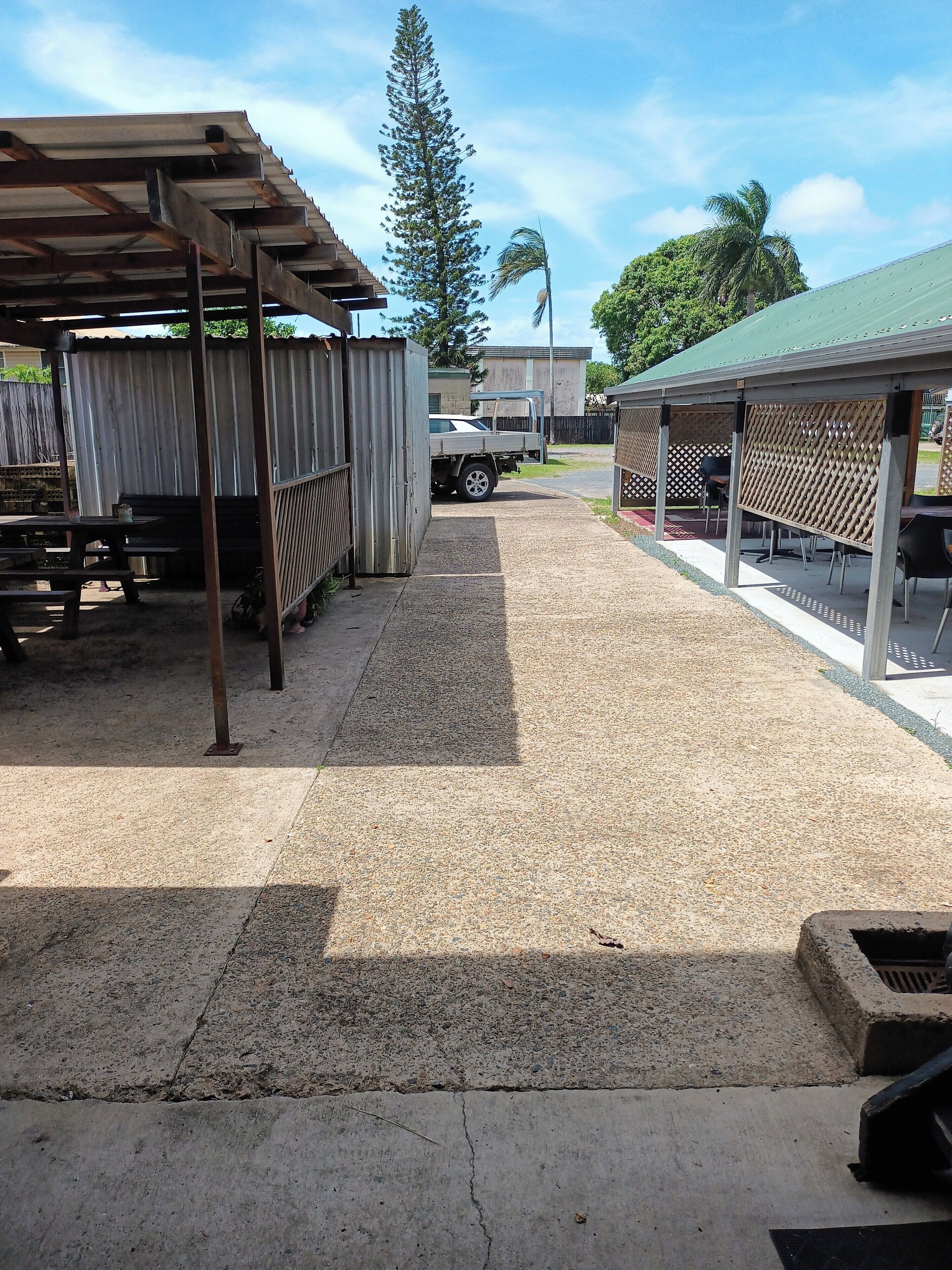 A covered outdoor area with picnic tables, a truck, and a building with a green roof.