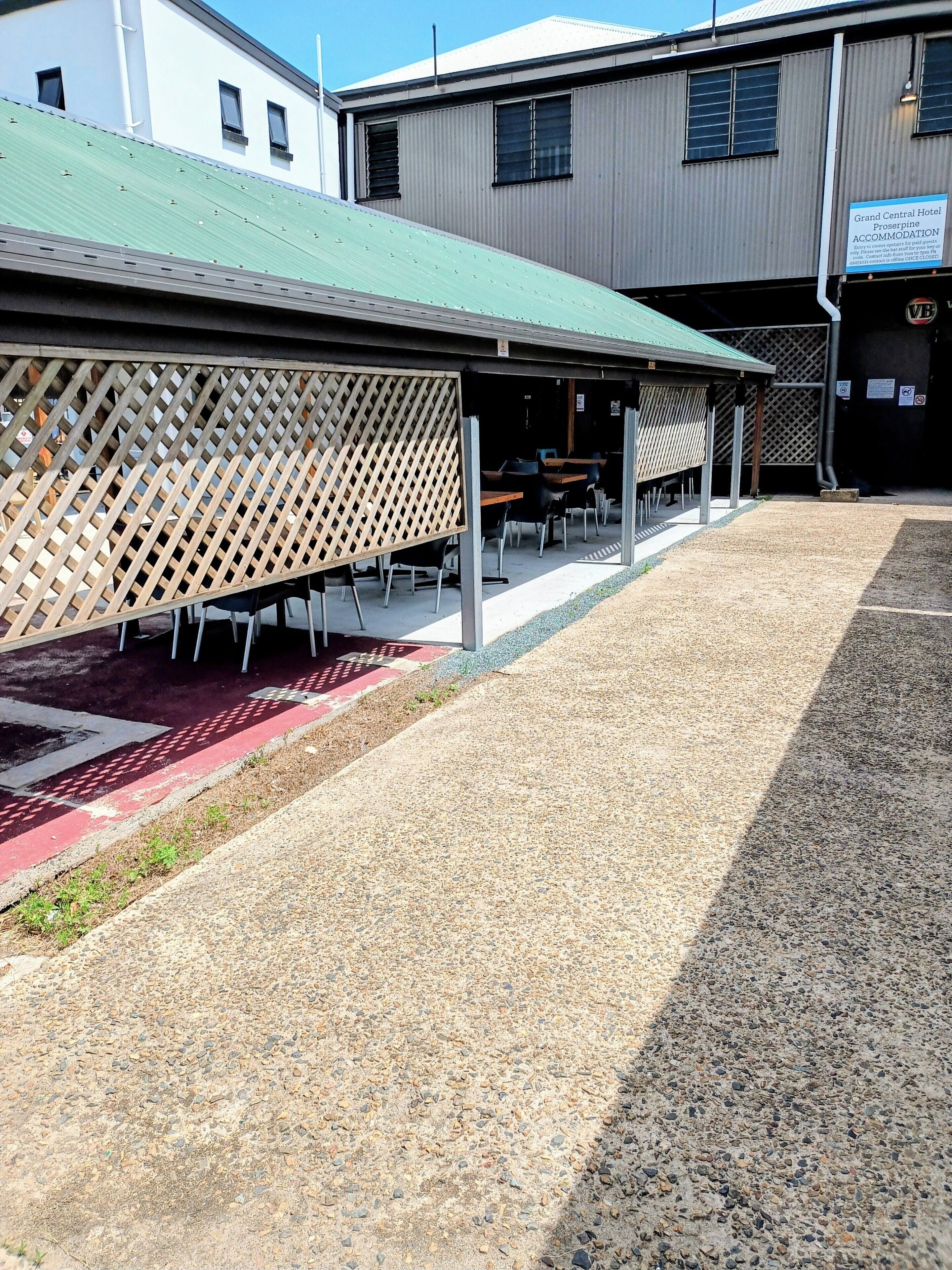 Un espace extérieur abrité, aménagé avec des tables et des chaises, un chemin de gravier et un bâtiment portant une enseigne indiquant qu'il s'agit d'un hôtel.
