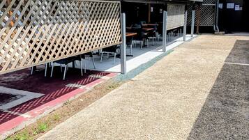 Un espace extérieur abrité, aménagé avec des tables et des chaises, un chemin de gravier et un bâtiment portant une enseigne indiquant qu'il s'agit d'un hôtel.
