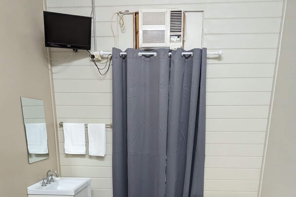 A small, clean room with a bed, a bedside table, a mirror, a sink, and a shower curtain.