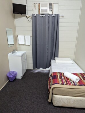 A small, clean room with a bed, a bedside table, a mirror, a sink, and a shower curtain.