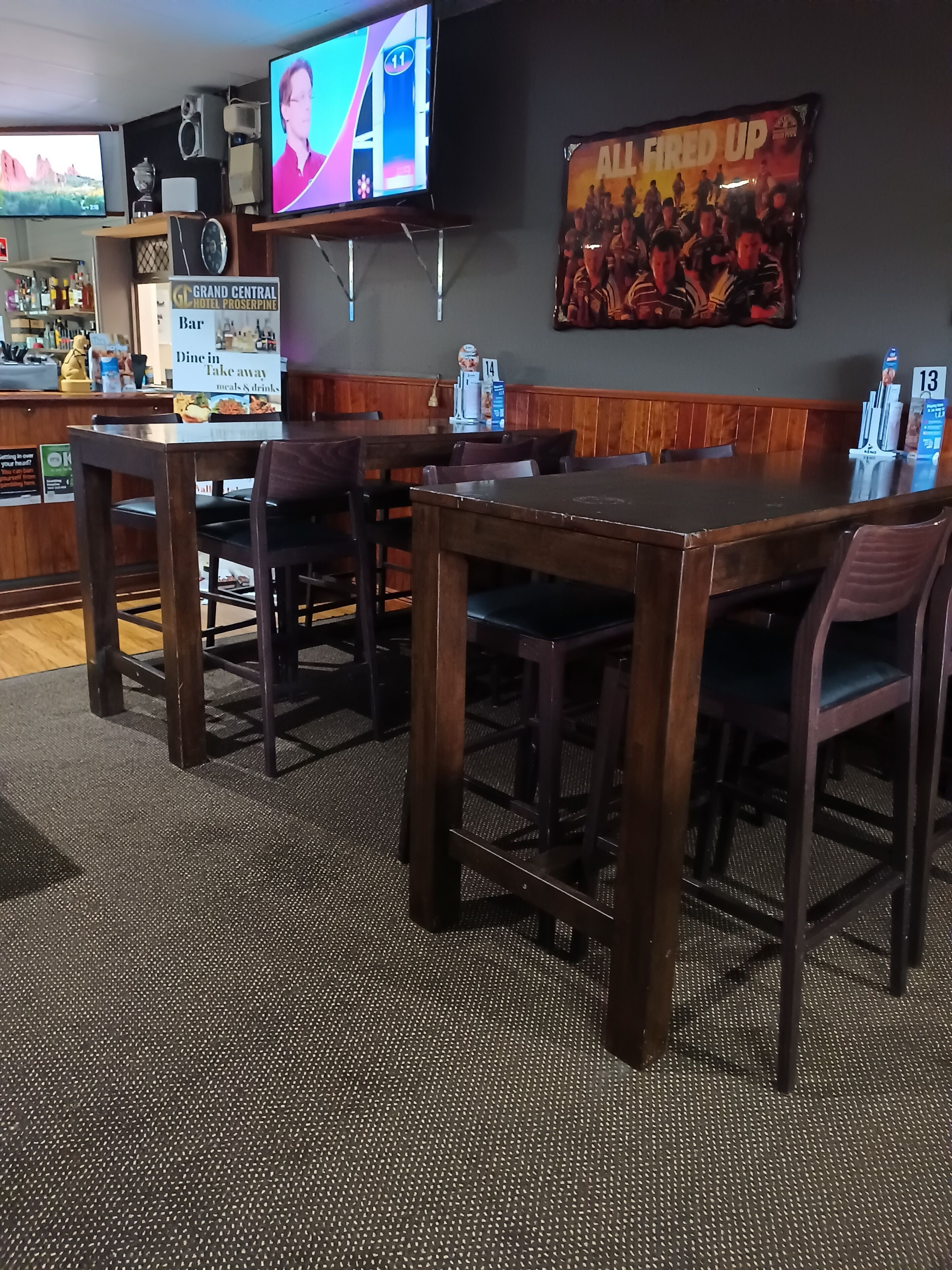A restaurant with wooden tables and chairs, a bar area, and a television mounted on the wall.