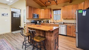 Una cocina con armarios de madera, un refrigerador de acero inoxidable, un microondas y una cafetera. Hay dos taburetes de bar y una isla de madera con un lavamanos.