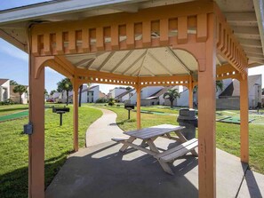 A gazebo with a picnic table, surrounded by a well-maintained lawn and a walking path.