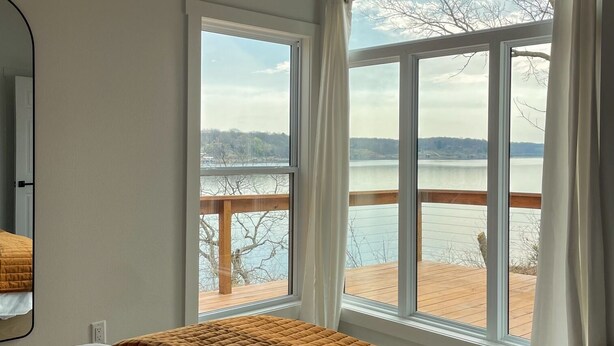 Une chambre à coucher avec un lit, une fenêtre donnant sur un lac et une terrasse, et un miroir sur le mur.