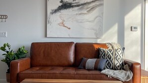 Un canapé en cuir marron, une table basse en bois devant, un grand tableau abstrait accroché au mur et une plante en pot sur la gauche.