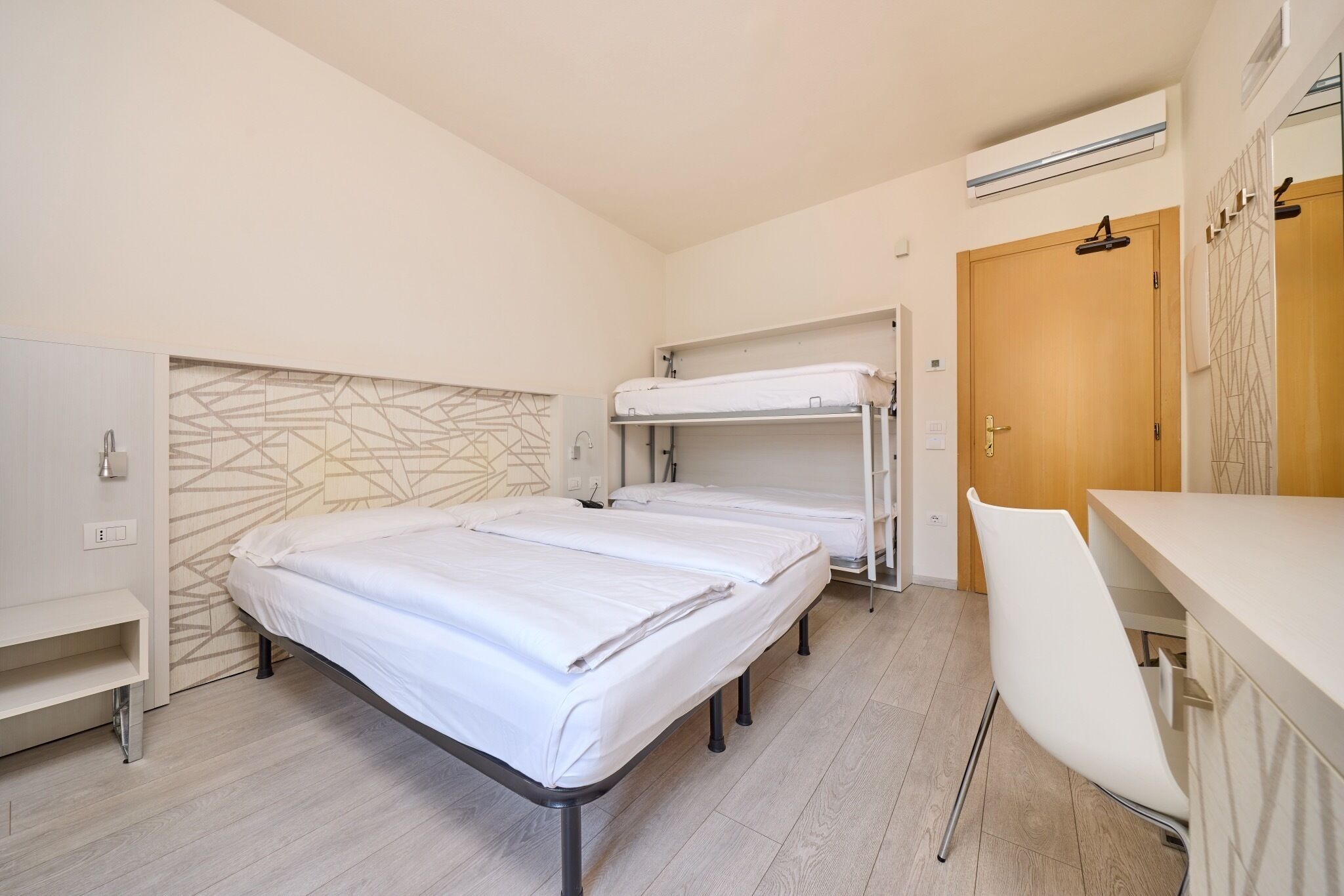A modern hotel room with bunk beds, a desk, and a chair.