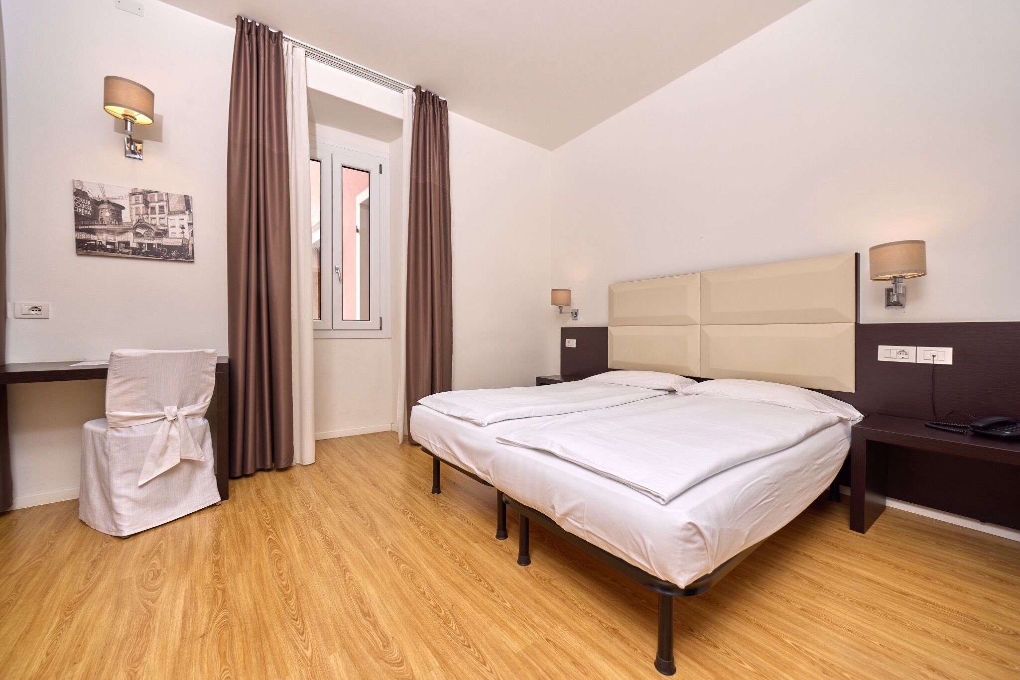 Een hotelkamer met een bed, een bureau, een stoel en een raam met gordijnen.
