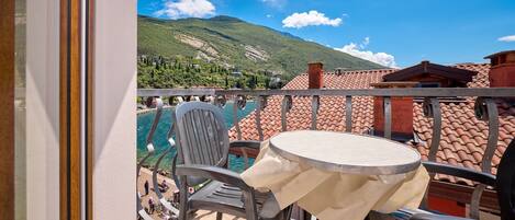 A balcony with a table and chairs, overlooking a mountainous landscape and a body of water.
