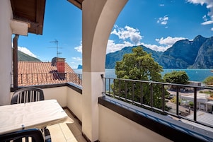 A balcony with a table and chairs, overlooking a mountainous landscape and a body of water.