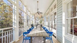 A covered porch with a wooden table and blue chairs, large windows, and a ceiling fan. - Seabbatical at WaterColor|Private Community Beach Access|On Western Lake (WaterColor)
