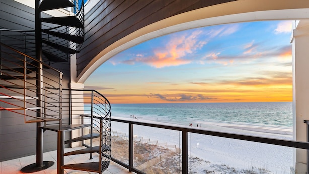 Una escalera moderna que lleva a un balcón con vista a una playa al atardecer.