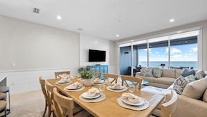 Un comedor con una mesa de madera dispuesta para seis personas, un aparador azul y un televisor montado en la pared.