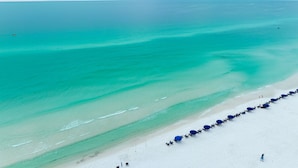 Una playa con aguas turquesas cristalinas y una hilera de sombrillas azules a lo largo de la orilla.