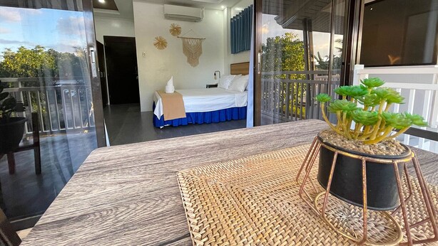Une chambre avec un lit, une petite table sur laquelle est posée une plante, et un balcon doté d’une balustrade.