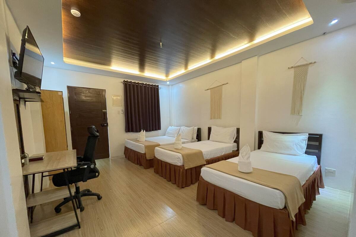 Een hotelkamer met drie enkele bedden, een bureau met stoel, een televisie en een houten vloer.
