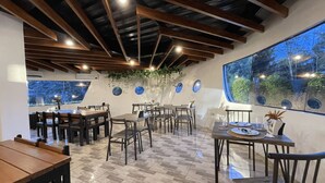L’intérieur d’un restaurant est agrémenté de tables et de chaises en bois, d’une grande fenêtre offrant une vue dégagée et d’un plafond avec des poutres apparentes.