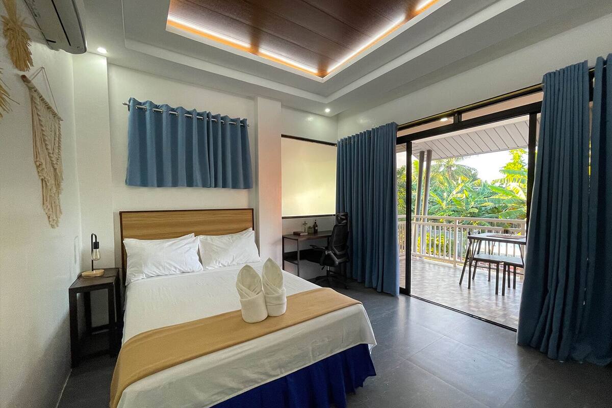 Een moderne hotelkamer met een bed, een bureau en een balkon met blauwe gordijnen.