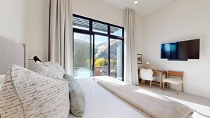 Un dormitorio moderno con una ventana grande, una cama, un escritorio y un televisor.