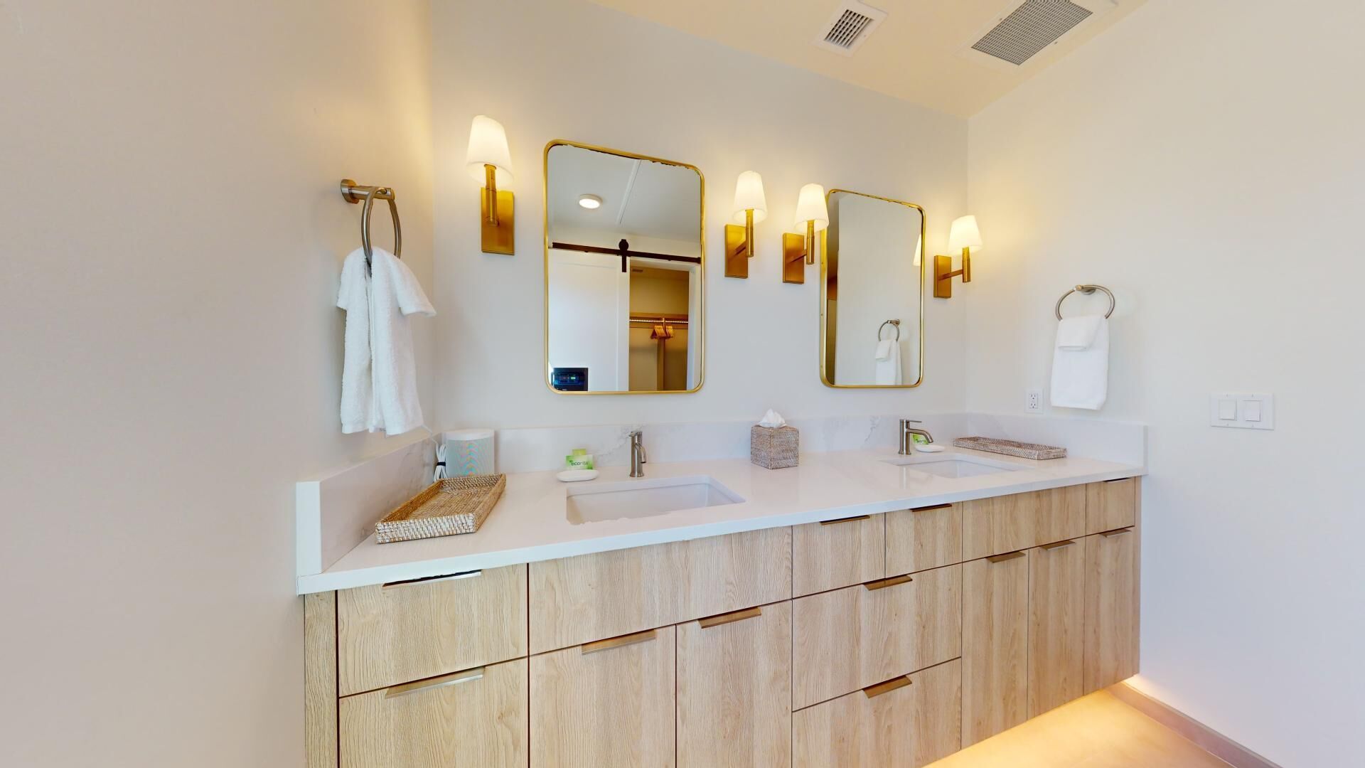 A modern bathroom with a white vanity, two mirrors with gold frames, and wall-mounted sconces.