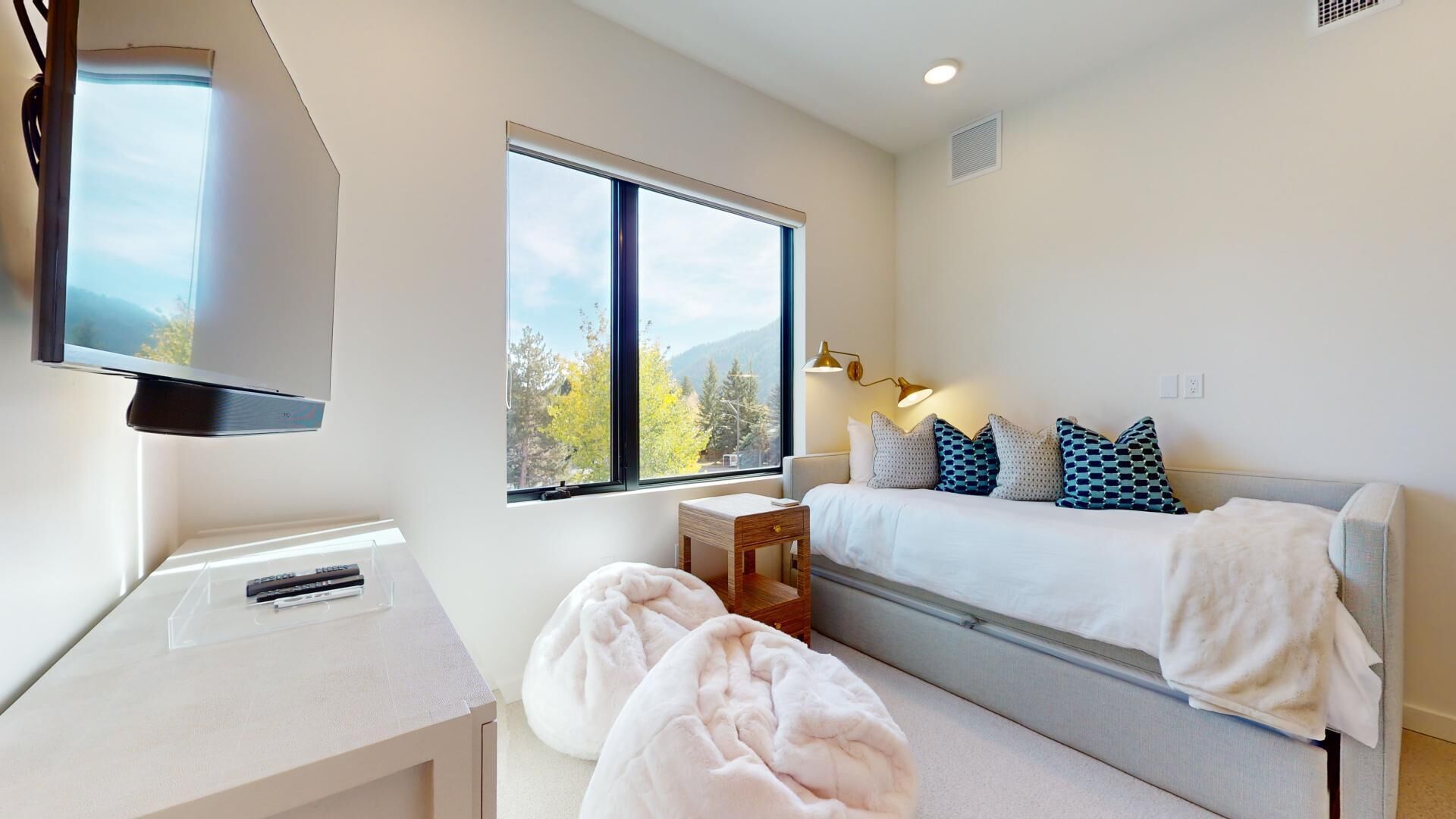 Un dormitorio moderno con un ventanal grande, una cama con almohadones estampados, una mesita de noche y un televisor sobre un mueble.
