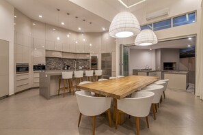 A modern kitchen with a central island, white wicker chairs, and pendant lighting. - Elegant BeachFront Villa w/ 4 king beds, gym, pool, breakfast & Housekeeping (Tamarindo)