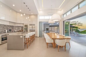 A modern kitchen with a central island, bar stools, and a dining table. - Elegant BeachFront Villa w/ 4 king beds, gym, pool, breakfast & Housekeeping (Tamarindo)