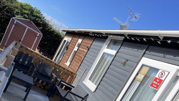 A wooden deck with outdoor furniture, a small building with a window and a door, and a sign prohibiting BBQs or fires. - 2 Bed Chalet Sleeps 4- Garden, Pets, Beach (Bridlington)