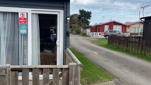A small wooden structure with a sign prohibiting BBQs or fires, a wooden fence, and a road with a car in the background. - 2 Bed Chalet Sleeps 4- Garden, Pets, Beach (Bridlington)