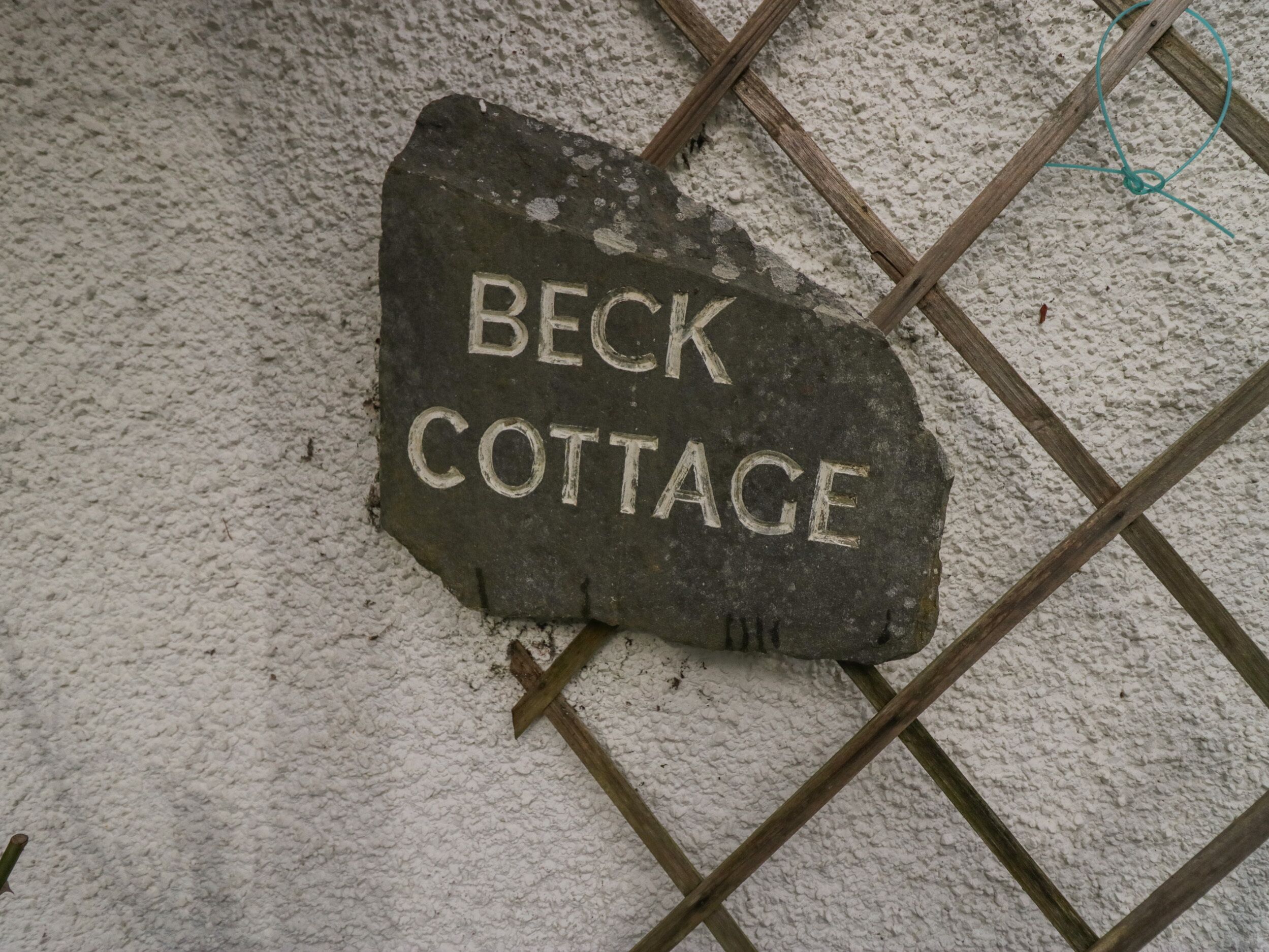 Un letrero de piedra con la inscripción 'BECK COTTAGE' en una pared con textura.