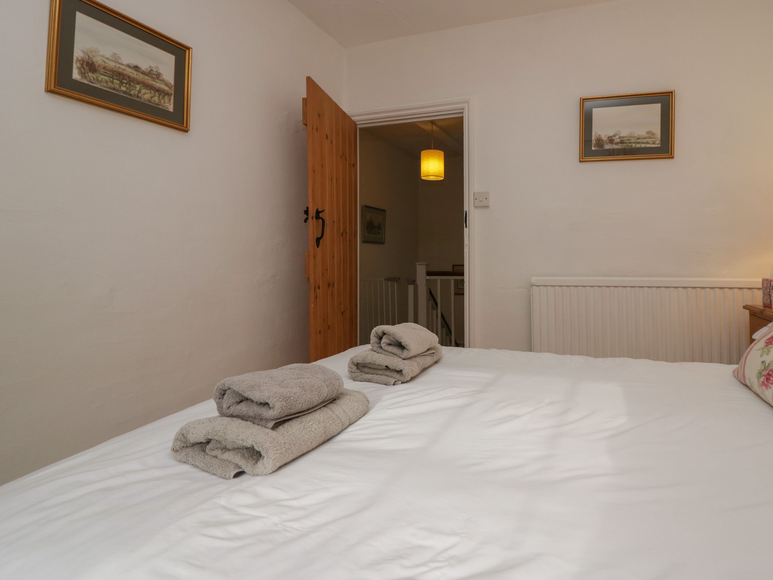 A bedroom with a bed, two towels, a wooden door, and two framed pictures on the walls.