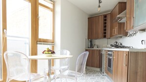 A modern kitchen with wooden cabinets, a gas stove, and a dining area with clear chairs and a table. - Apartment With Canal View in Broadway Market (London)