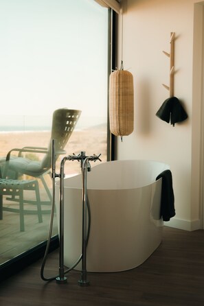 A modern bathroom with a freestanding bathtub, a wicker basket, and a black lamp on the wall. - Espazo (Carballo)