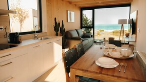 A modern kitchen with a wooden countertop, a dining table set with plates, and a view of the beach through large windows.