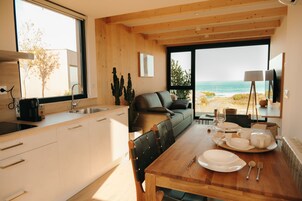 A modern kitchen with a wooden countertop, a dining table set with plates, and a view of the beach through large windows.