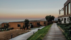 A modern building with a wooden facade, a pathway leading to a grassy area, and a view of the ocean.